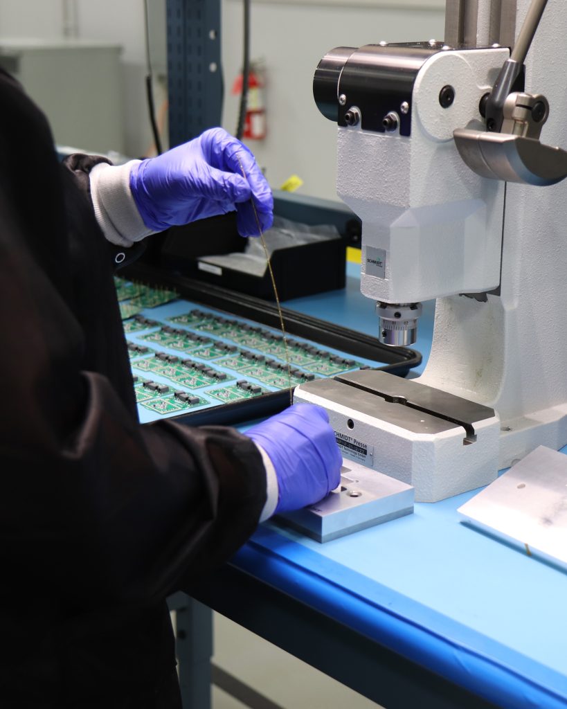 An employee wearing purple gloves handles equipment used to produce microchips.